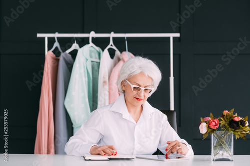 Successful senior business woman. Fashion stylist. Smart elderly lady busy browsing tablet and making notes in day planner. Office workspace. photo