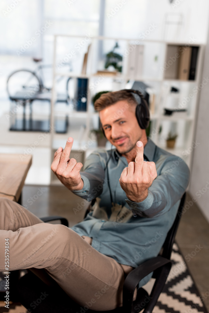Fototapeta premium selective focus of cheerful man showing middle fingers while listening music in headphones