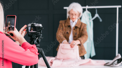 Fashion stylist assistant. Successful blogging business. Confident senior lady shooting video tutorial on latest trends. photo