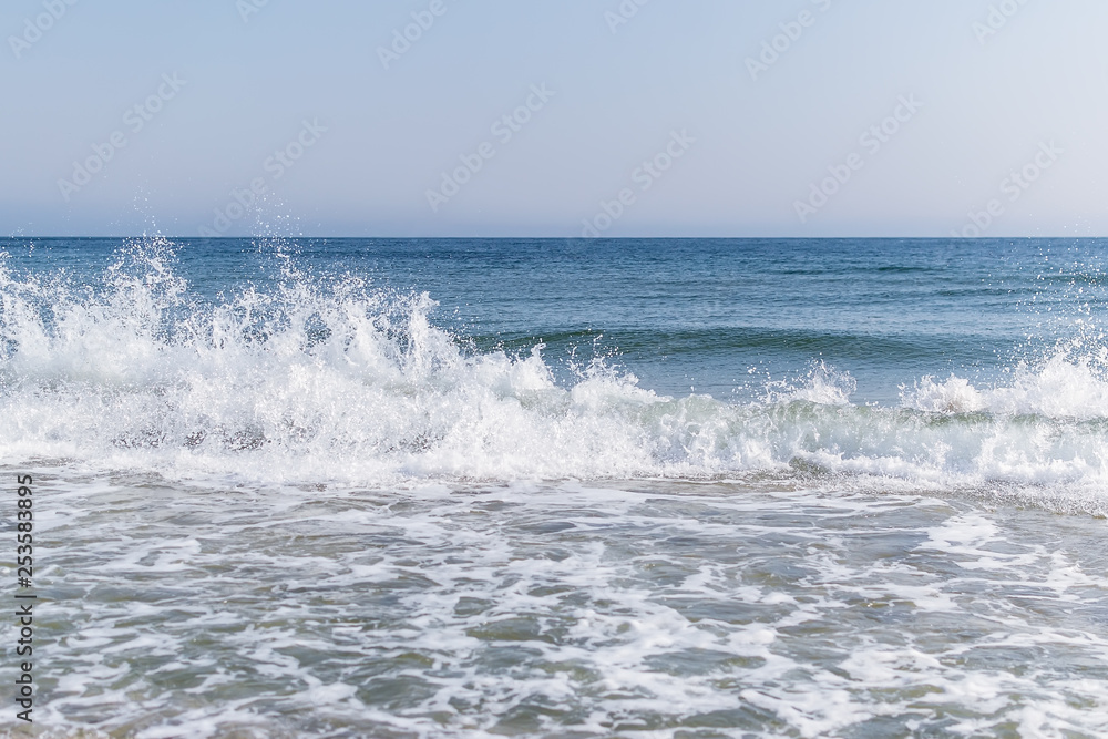 Sea surf with white foam and spraying water drops in the air. Seascape of Black Sea in February on a sunny day.