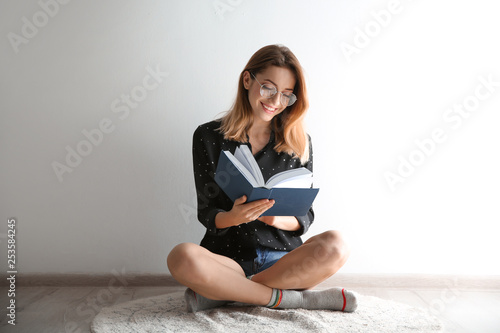 Young woman reading book on floor near wall