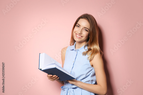 Young woman with book on color background, space for text