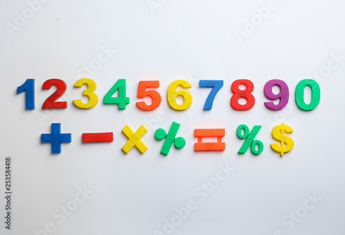 Colorful magnetic numbers and math symbols on white background  top view