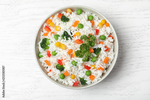Bowl with tasty rice and vegetables on wooden background, top view