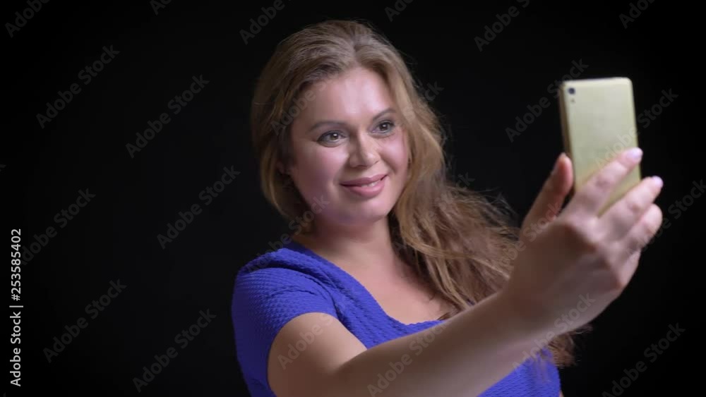 Closeup shoot of adult caucasian female taking selfies on the phone smiling and posing in front of the camera Closeup shoot of adult caucasian female taking selfies on the phone smiling and posing in front of the camera