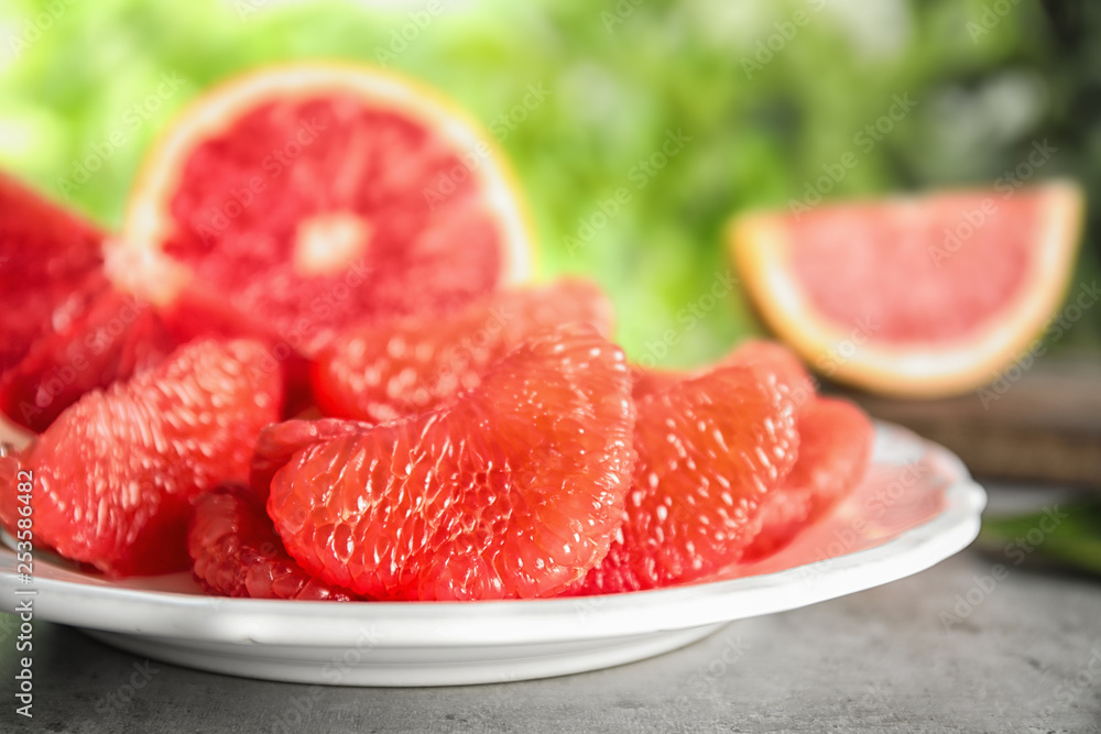 Plate with ripe grapefruit on table against blurred background Plate with ripe grapefruit on table against blurred background