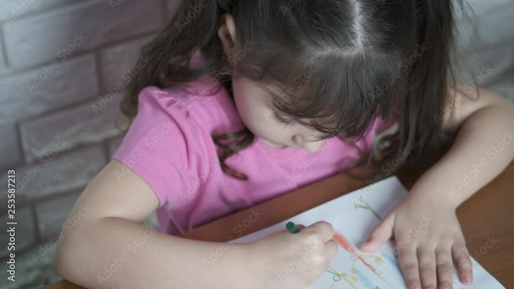 The child draws with crayons. A cute little girl draws with seven colored crayons, top view. The child draws with crayons. A cute little girl draws with seven colored crayons, top view.