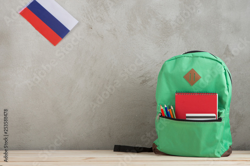 Φωτογραφία green backpack, flag of the Russia, chancellery and notebooks against a cement w
