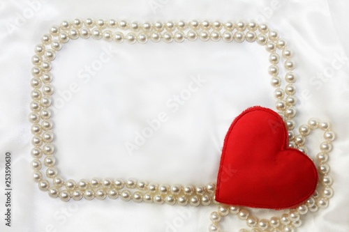 Silk white textile material background with glossy beads frame and textile heart decor in corner