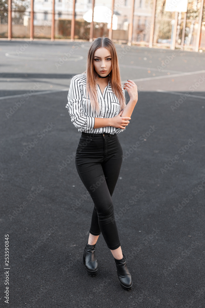Glamorous modern young woman in black stylish jeans in a striped elegant  blouse in trendy leather