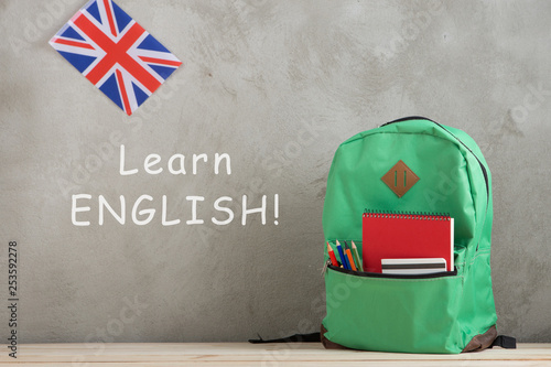 backpack, flag of the Great Britain and notebooks against a cement wall with text "Learn English!"