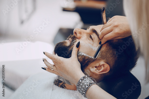 handsome young bearded guy sitting in an armchair in a beauty salon and the girl near him shrugs his neck
