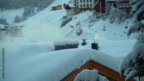 A smoking chimney on the snow-covered rooftop in the village of Samnaun, Switzerland. Slow motion, 120fps. photo