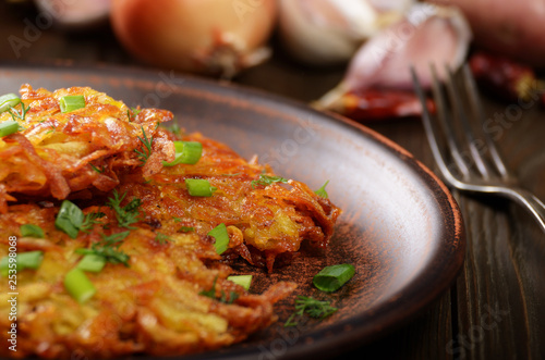Fresh homemade tasty potato pancakes in clay dish with vegetables on wooden table
