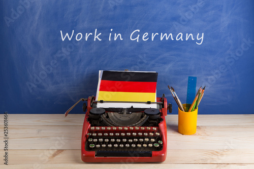 work abroad concept - red typewriter, flag of Germany on table and blackboard with text 