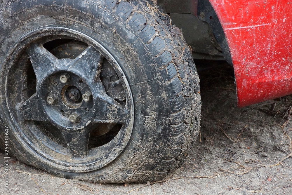 black flat tire of a red car on a dirt road