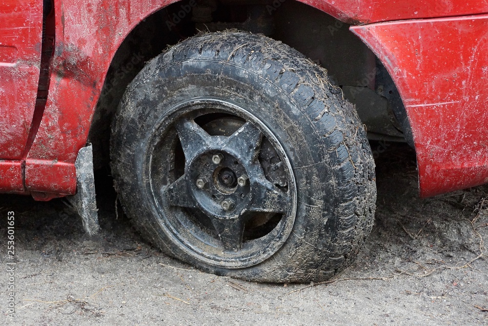 one black flat tire of a red car on a dirt road