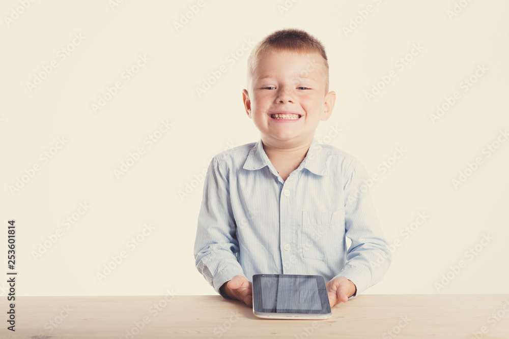 Happy little boy in suit sitting at table with tablet gadget. Children portrait. Back to school. Stylish man in fashionable suit shirt and pants with blue eyes Happy little boy in suit sitting at table with tablet gadget. Children portrait. Back to school. Stylish man in fashionable suit shirt and pants with blue eyes