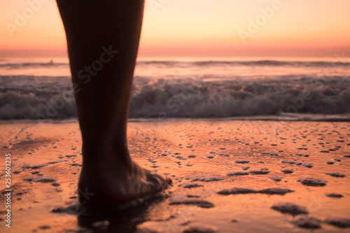 Leg of a young person who is watching the sunset in the beach