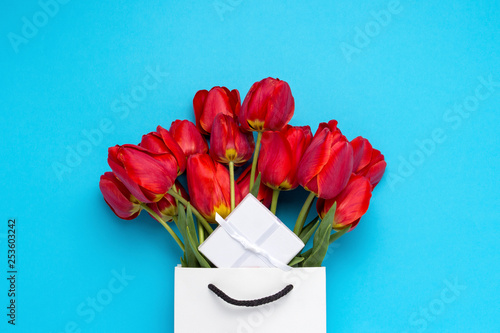 White Gift Bag, a small white gift box and a bouquet of red tulips on a blue background. Concept Offers an engagement or marriage, shopping