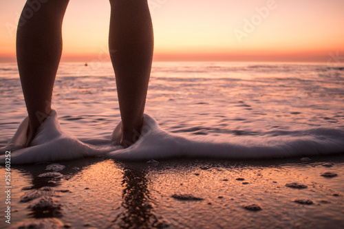 Legs of a young person who is watching the sunset in the beach