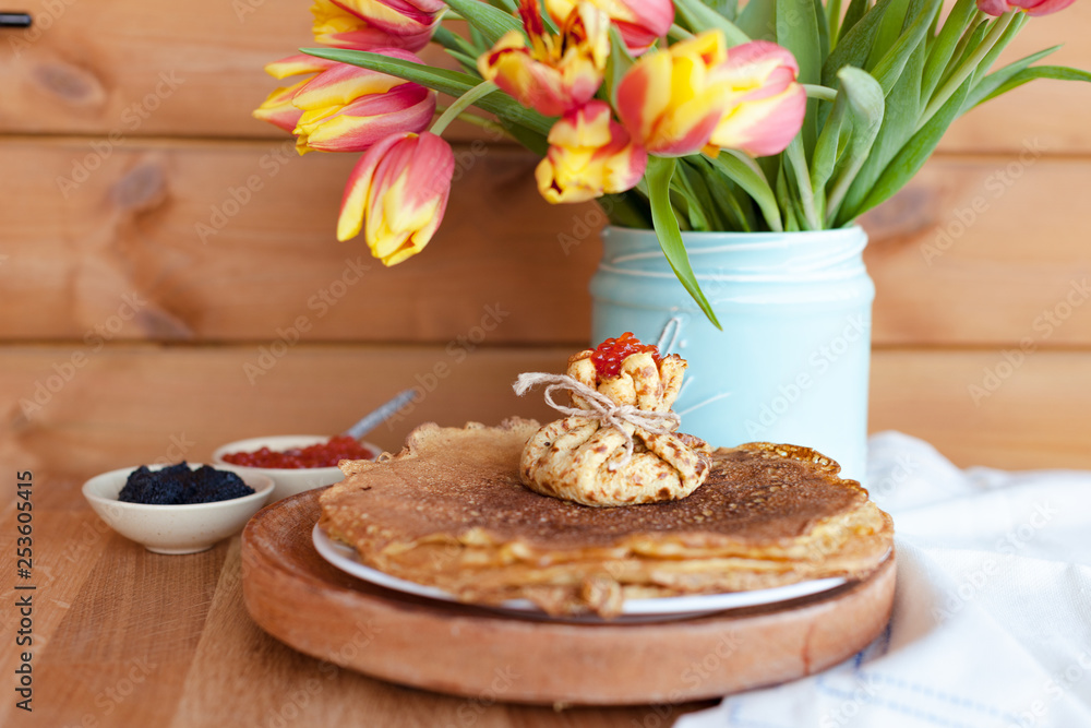 Large round pancakes with red and black caviar. Envelopes from pancakes with filling. A bouquet of fresh spring tulbpans on the table and breakfast. Fotov rustic style. Copy space.