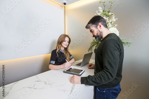 Beautiful young woman attending a customer at the reception of a clinic. She is pointing information on the tablet.