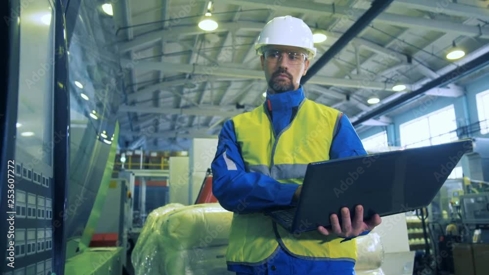 Factory worker with a laptop is observing a digital display Factory worker with a laptop is observing a digital display