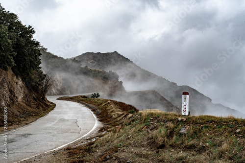 A wet and winding road running through mountains and fog  photo