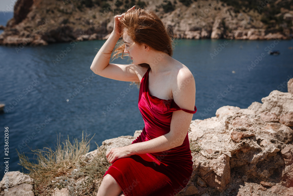 A beautiful red-haired woman is sitting on a rock A beautiful red-haired woman is sitting on a rock