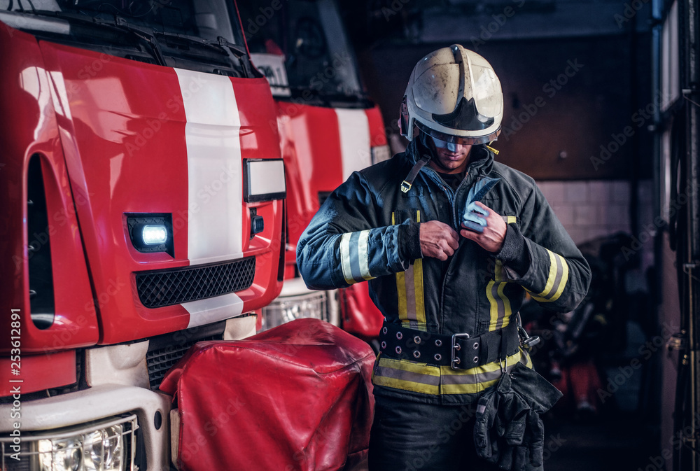 Fototapeta premium Fireman clothes protective uniforms standing next to the fire engine in the garage of a fire department