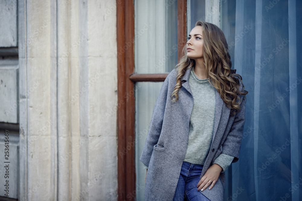 Fototapeta premium Fashion model wearing ripped boyfriend jeans, jacket and sneakers posing in the city