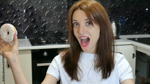 Closeup portrait of funny girl with long hair having fun with red and white donuts against her eyes at the kitchen at home