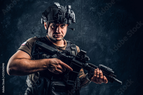 Brutal soldier of the Russian Federation wearing body armor and helmet with a night vision posing with an assault rifle. Studio photo against a dark textured wall  photo