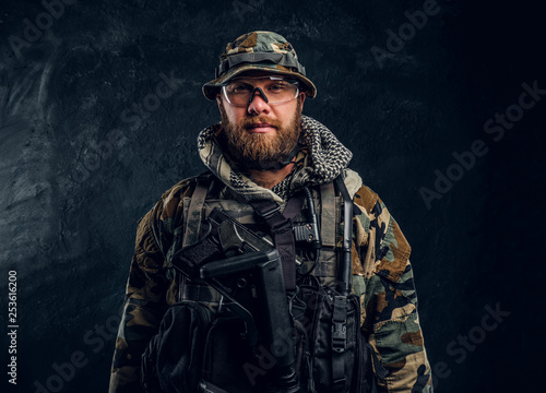 Portrait of a special forces soldier in the military camouflaged uniform, looking at a camera. Studio photo against a dark textured wall