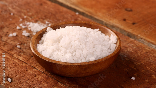 Salt or sea salt in a wooden bowl on a aged wooden table background.