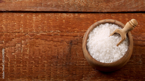 Salt or sea salt in a wooden bowl on a aged wooden table background.