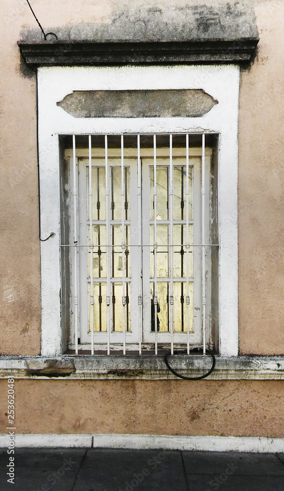 Old window with metal frame and white bars on a worn wall
