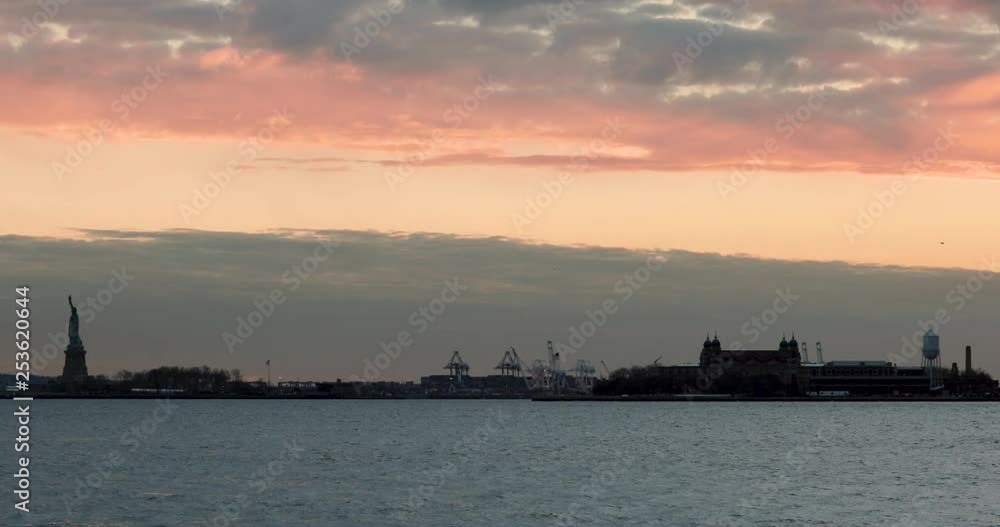 Static shot of the Statue of Liberty and Ellis Island silhouetted against sunset skies. Static shot of the Statue of Liberty and Ellis Island silhouetted against sunset skies.