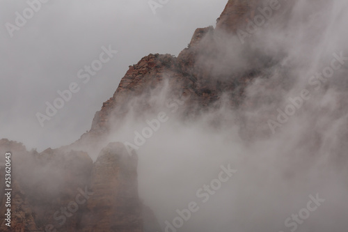Red sandstone mountains are partially revealed as rain clouds swirl around the peaks in Zion national park Utah. 