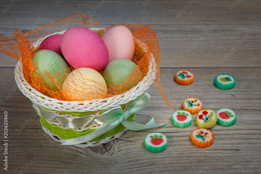 Fototapeta premium Multi-colored Easter eggs and sweets in a beautiful basket.