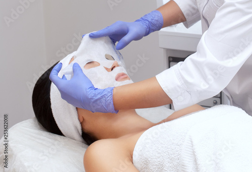 The cosmetologist for procedure of cleansing and moisturizing the skin, applying a sheet mask to the face.Cosmetology and professional skin care.