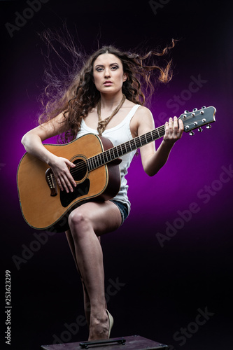 Young woman with guitar, isolated on black and violet background.