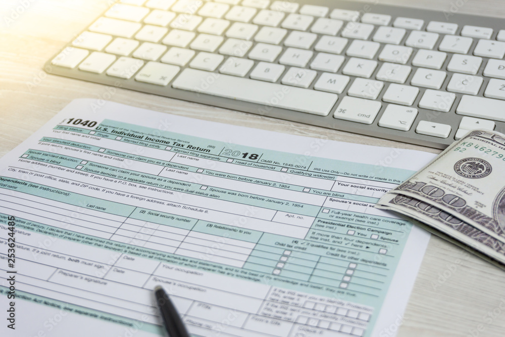 US tax form next to computer keyboard and tax form 1040. tax form us business income office hand fill concept US tax form next to computer keyboard and tax form 1040. tax form us business income office hand fill concept