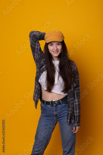 Excited young hipster woman in casual dress, widely smiling, looking at camera. Isolated on yellow background