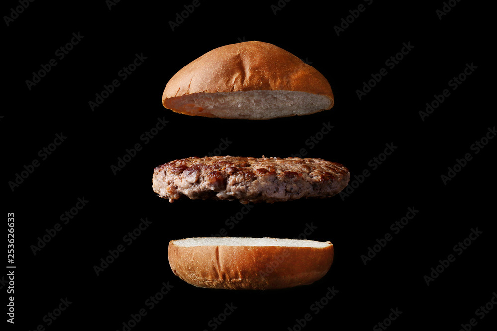 Naklejka premium flying burger with bun and patty isolated on black background
