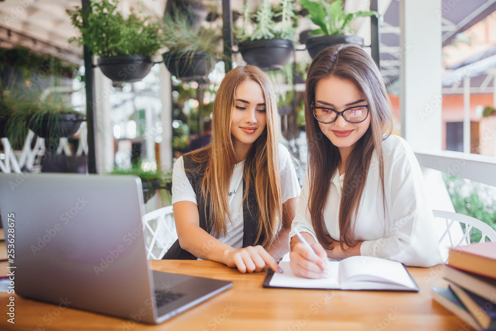 Two young beautiful businesswoman people discussing the terms of the contract sitting at the office table with laptop Two young beautiful businesswoman people discussing the terms of the contract sitting at the office table with laptop