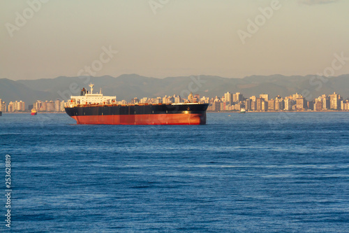 Giant Bulk cargo ship far away at achorage with beautiful city on background photo