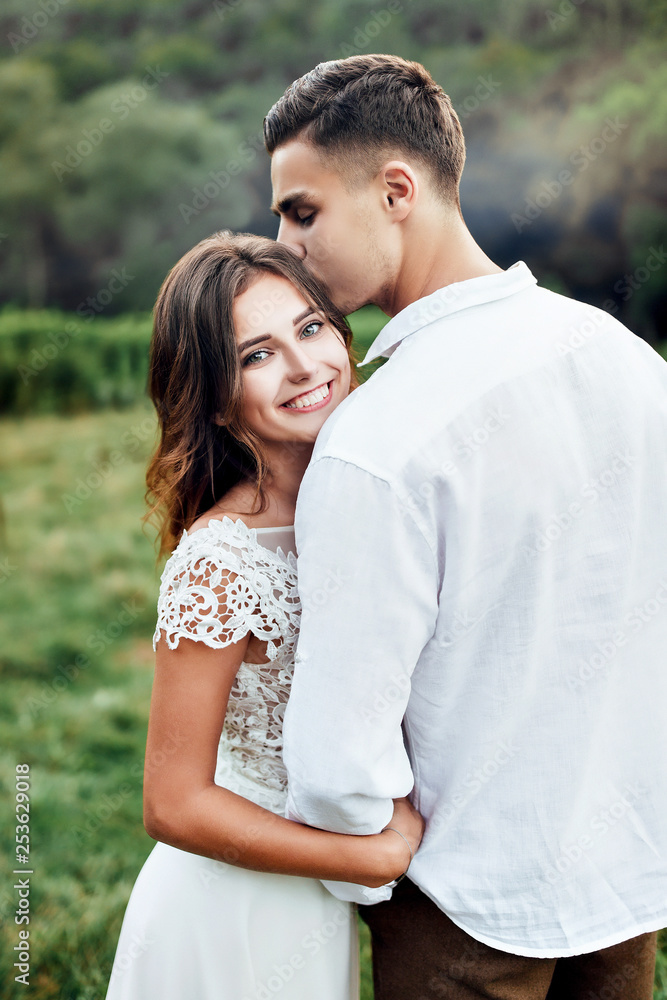 The groom kisses the bride and holds her waist. The bride grasped his neck with his hands. The groom kisses the bride and holds her waist. The bride grasped his neck with his hands.