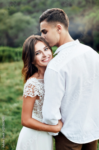 The groom kisses the bride and holds her waist. The bride grasped his neck with his hands.